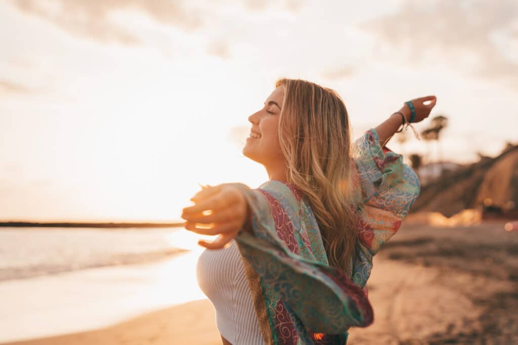 Junge Frau mit offenen Armen am Strand, die den Moment genießt; symbolisch für die Befreiung von emotionalen Lasten und die Selbstfindung durch psychologisches Coaching von Kindheitstraumata.