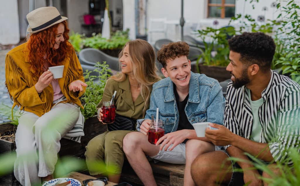 Gruppe junger Menschen, die im Freien in entspannter Atmosphäre zusammensitzen und lächeln; symbolisch für die positive Wirkung von psychologischem Coaching bei der Bewältigung von Kindheitstraumata.